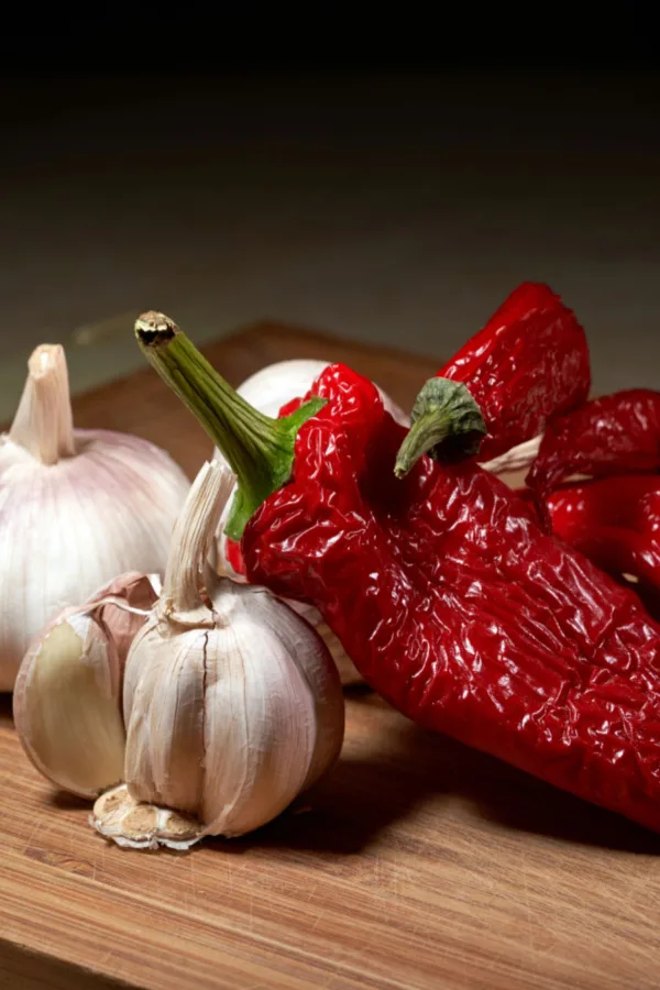 Garlic and hot peppers sitting on a wooden tray. Homemade hot pepper spray is a great way to protect plants from grasshoppers.