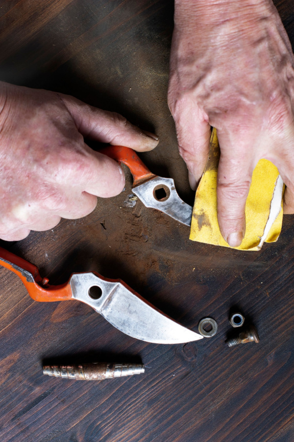 A man's hands cleaning a disassembled garden tool .