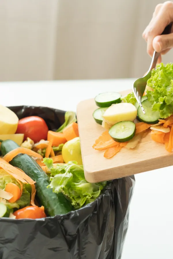 A lady moving vegetable kitchen scraps into a bucket. 