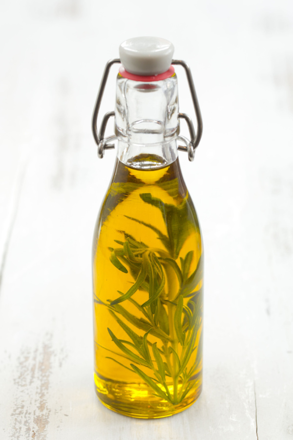 A jar with rosemary infused oil on a white table