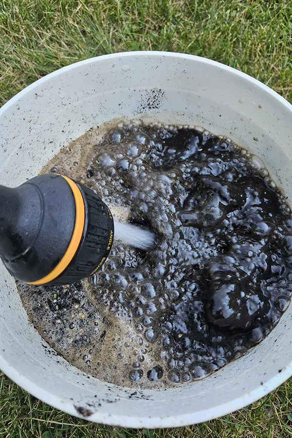 Water being added to a white bucket with compost already in it. 