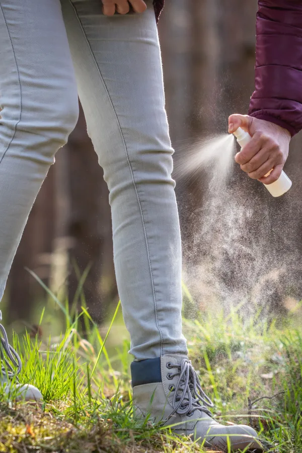 Someone spraying homemade tick spray on their jeans.