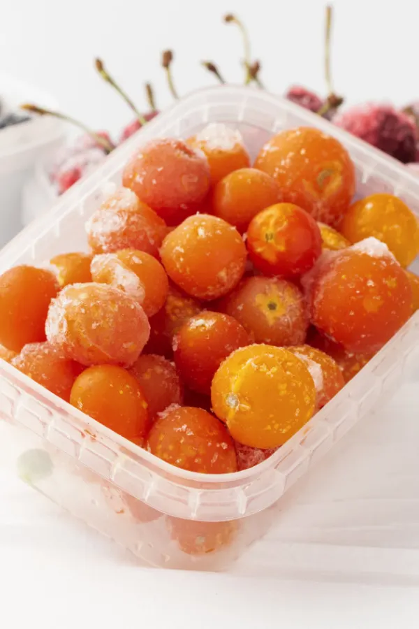 A plastic container full of frozen cherry tomatoes.