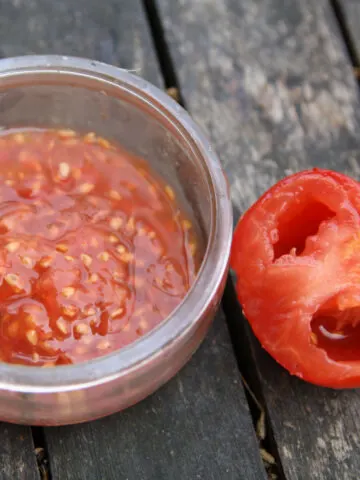 A jar of tomato seeds and pulp next to an empty tomato
