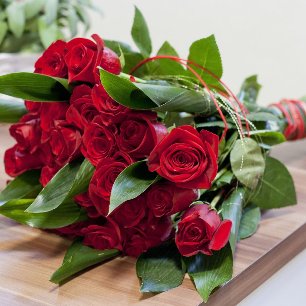 A bouquet of red roses laying on a wooden table. The stems can be propagated to create new rose bushes