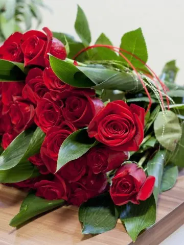 A bouquet of red roses laying on a wooden table.